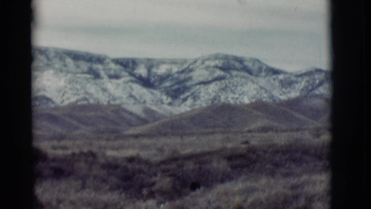 Snow-dusted mountains beyond open scrubland under a pale sky.