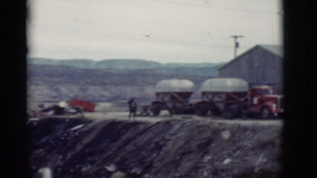 Garage yard with tank trailers, red truck, and a distant person near mountain terrain.