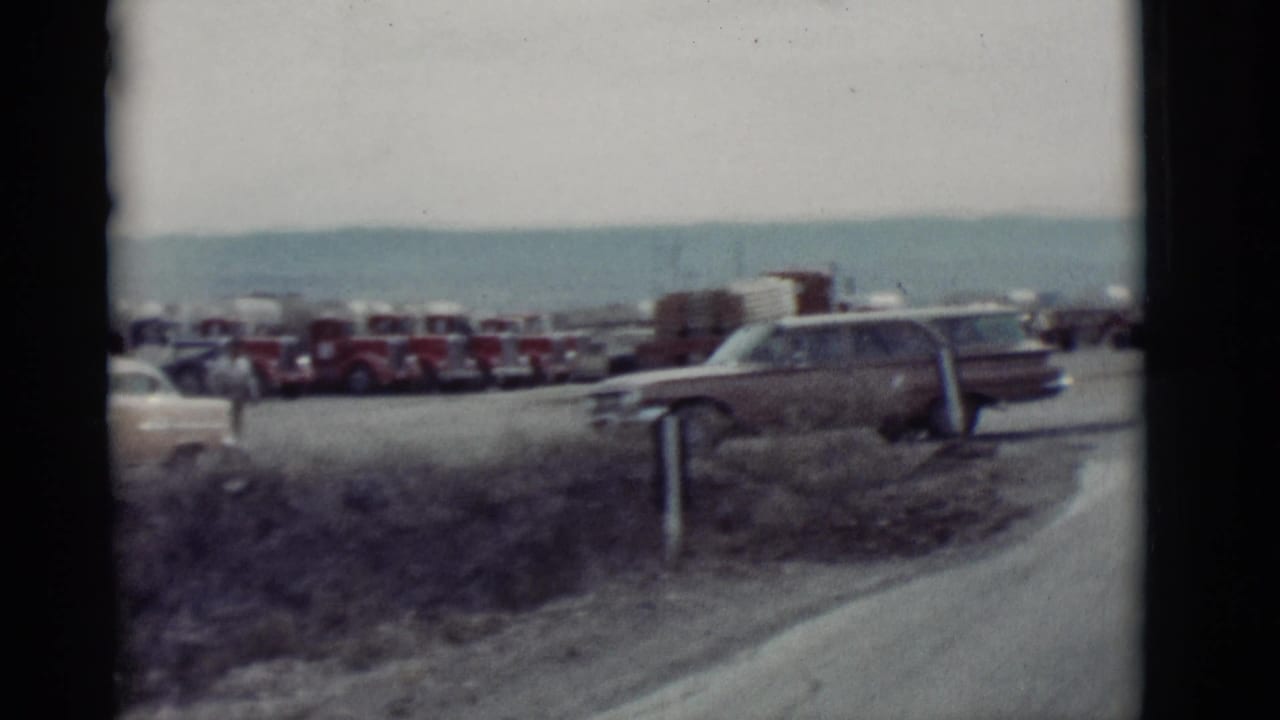 Parked cars beside a road with water or sky in the distance and dark film-frame edges.