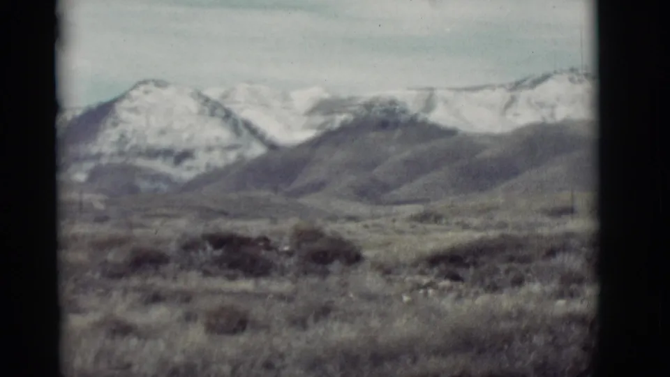 1964 New Mexico home-movie view of distant snow-capped mountains, low scrub, and open desert terrain with faded color.