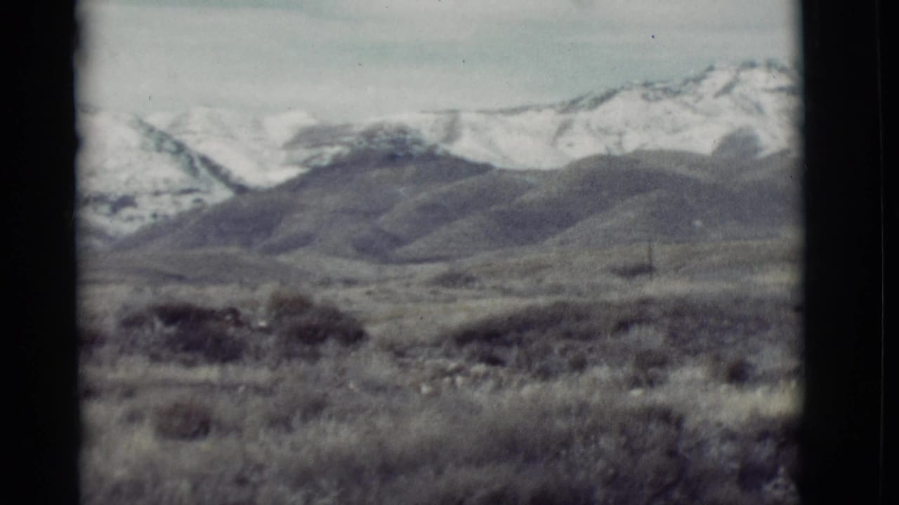 Wide view of scrubland, low hills, and distant snowy mountain ridges.