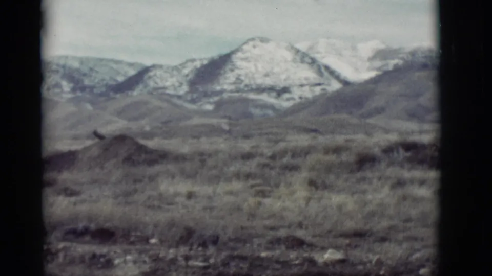 1964 New Mexico 8mm still with soft grain, dry brush, and distant snow-covered mountain peaks.