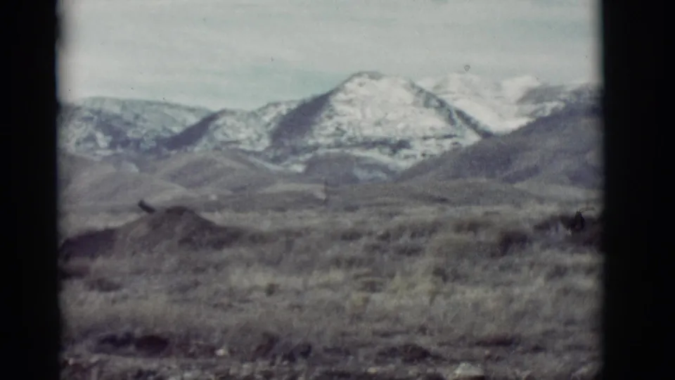 1964 New Mexico frame showing an arid foreground and bright snowy peaks within visible 8mm gate edges.