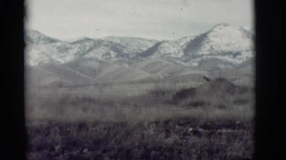 1964 New Mexico 8mm frame with a blurred arid foreground, low hills, and a snow-dusted mountain range.