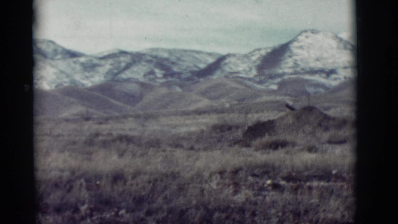 Dry grassland and rolling hills with snow-covered mountains in the distance.