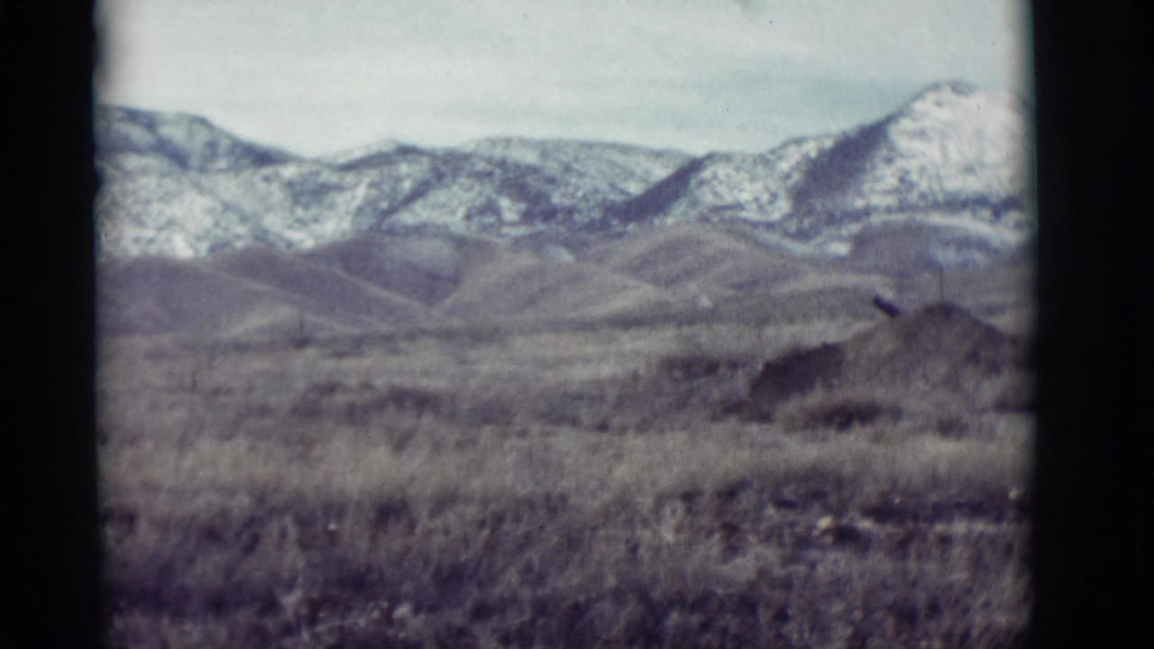 Snowy mountain range beyond low hills and dry open grassland.