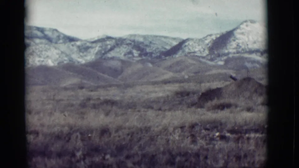 1964 New Mexico home-movie view of scrubby grassland, rounded hills, and distant snow-covered mountains with slight handheld softness.