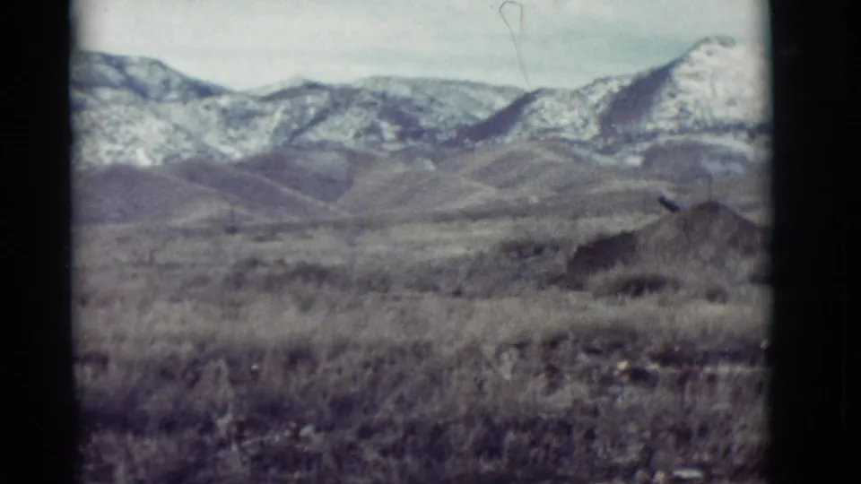 New Mexico 1964 8mm frame showing dry grasses, low hills, and a snow-covered mountain horizon with visible film wear.