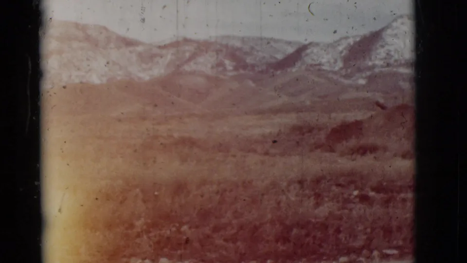 Faded 1964 New Mexico 8mm frame showing open desert terrain, low hills, distant mountains, and film scratches.
