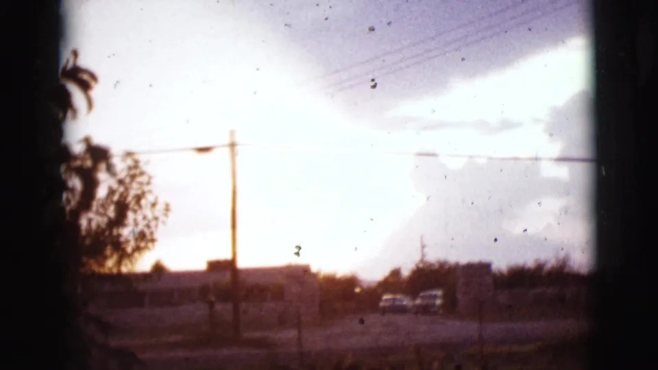 Arizona roadside view with a utility pole, overhead wires, cars, and a bright break in storm clouds.