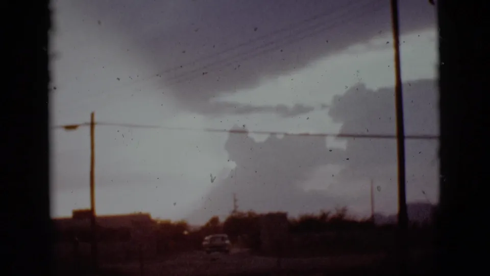 A road scene in Arizona shows a car near utility poles and wires, with a large storm cloud dominating the sky.