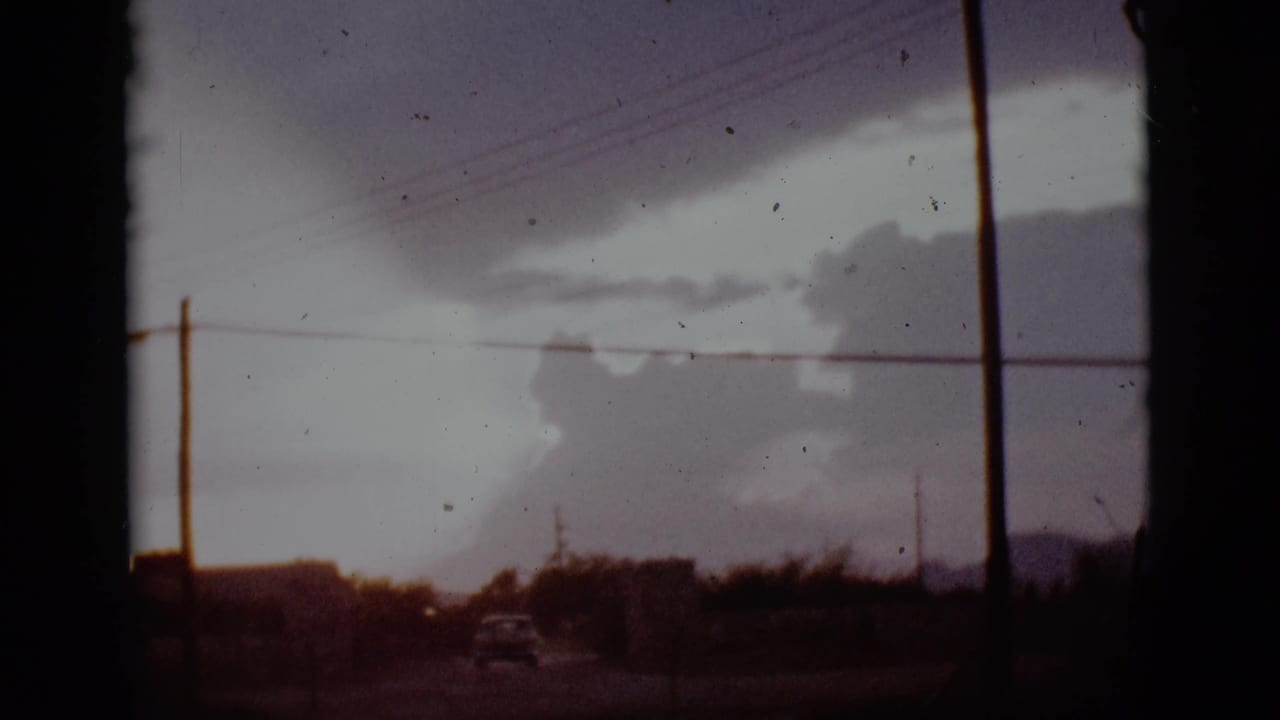 Storm clouds over a rural road with power lines and a distant car.
