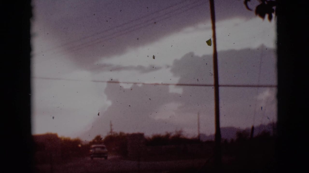 Distant car on a road beneath dark clouds and crossing power lines.
