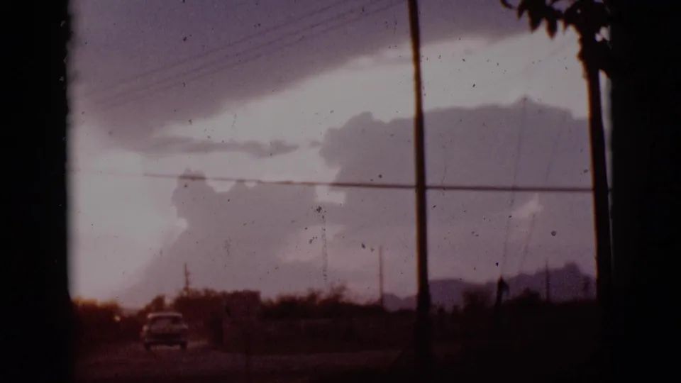 1965 Tuscon, Arizona 8mm frame showing a lone car near the lower edge, a tall utility pole, and layered storm clouds.