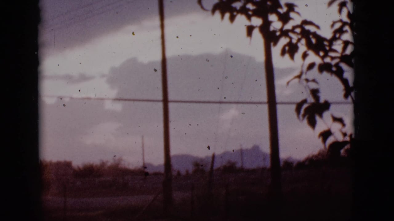 Clouds over distant mountains with utility poles, wires, and dark foreground branches.