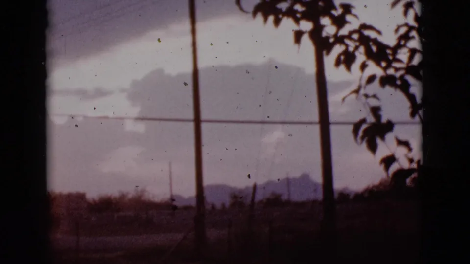 1965 Tucson-area road-view frame showing a purple sky, distant mountains, utility poles, overhead wires, and silhouetted branches.