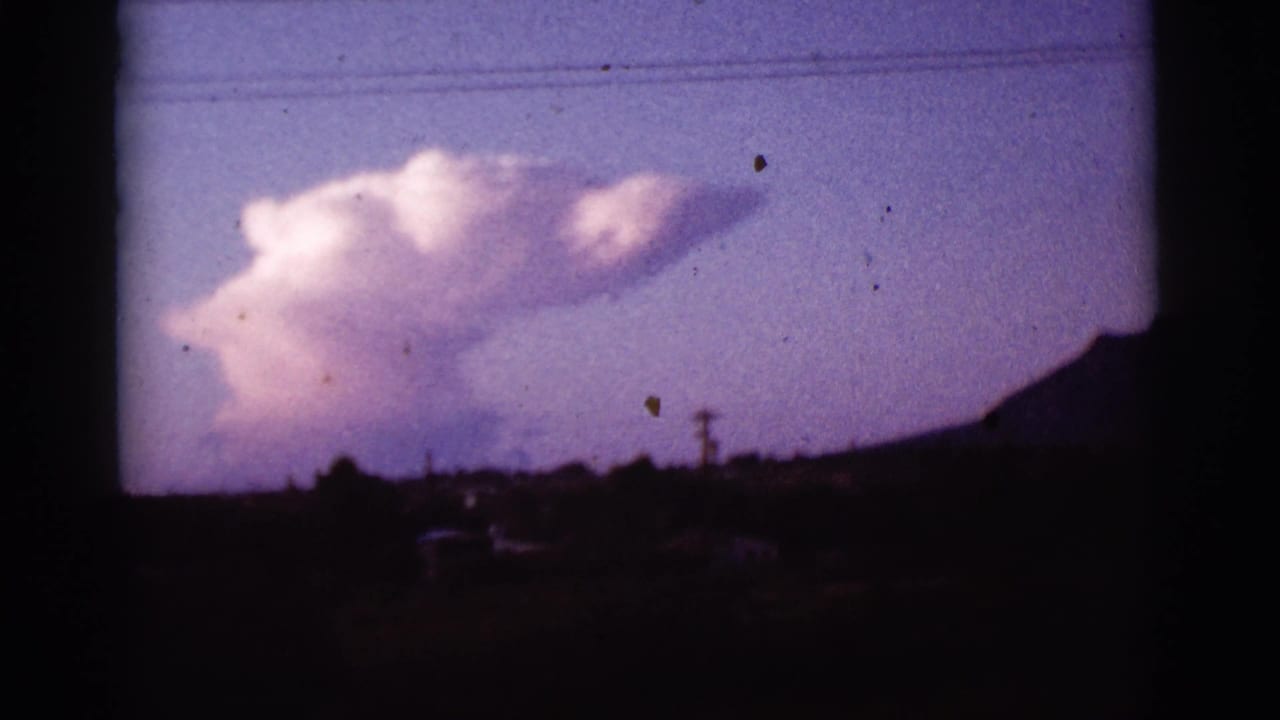Large pale cloud above a dark hillside and low utility lines at twilight.