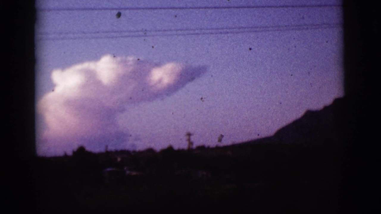 Pink-white cloud in a purple sky above silhouetted hills and a utility pole.