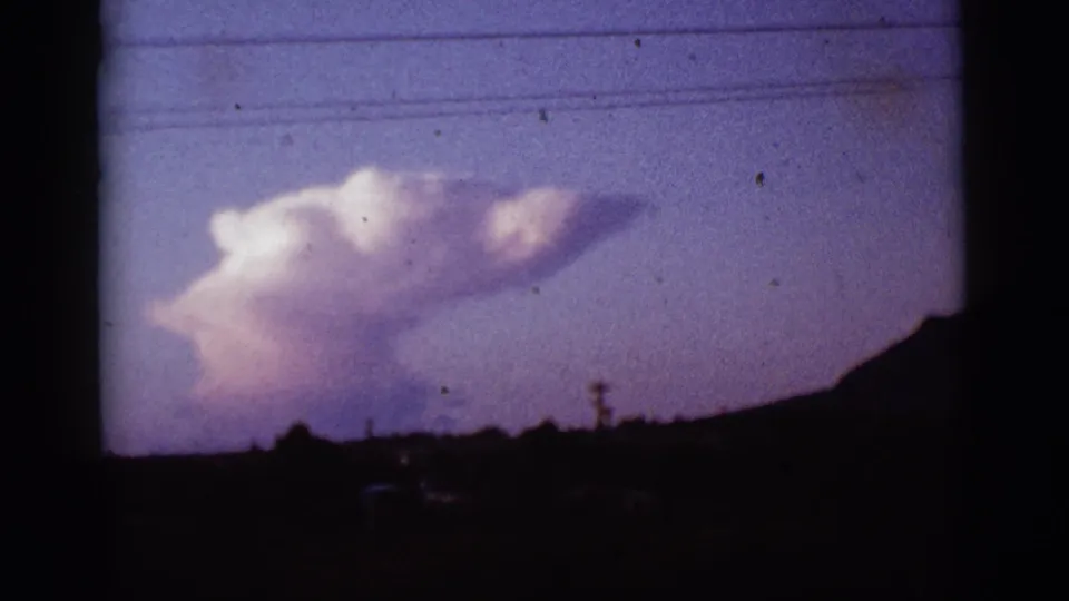 1965 Tucson-area home-movie frame showing a pale cloud against a faded twilight sky above a dark horizon.