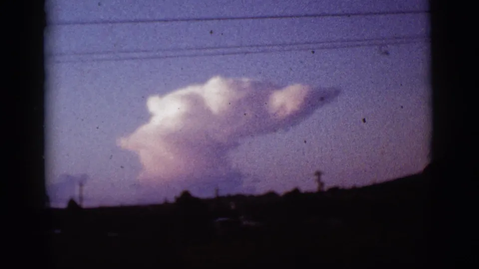 1965 Tucson, Arizona 8mm frame showing a large pale smoke cloud rising beyond a silhouetted horizon and utility lines.
