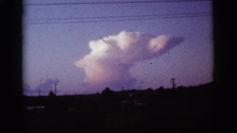 1965 Tucson, Arizona 8mm view of a bright smoke plume over distant structures and utility lines at the horizon.