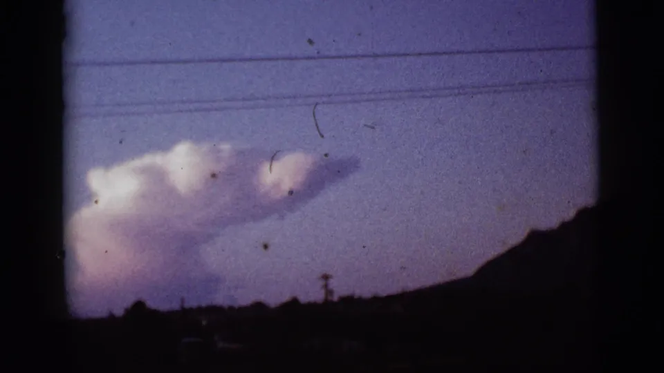 1965 Tucson, Arizona 8mm frame showing the smoke plume partly lower in frame beside a dark sloped horizon and wires.