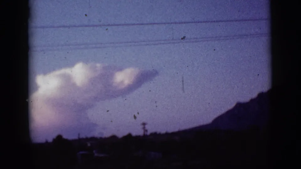 1965 Tuscon, Arizona 8mm frame showing a large cloud above a shadowed hill, with utility lines across the sky and film gate edges visible.