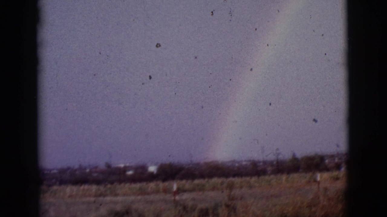 1965 8mm view of a faint rainbow over open land near Tucson, Arizona, with dark frame borders and visible film dust.