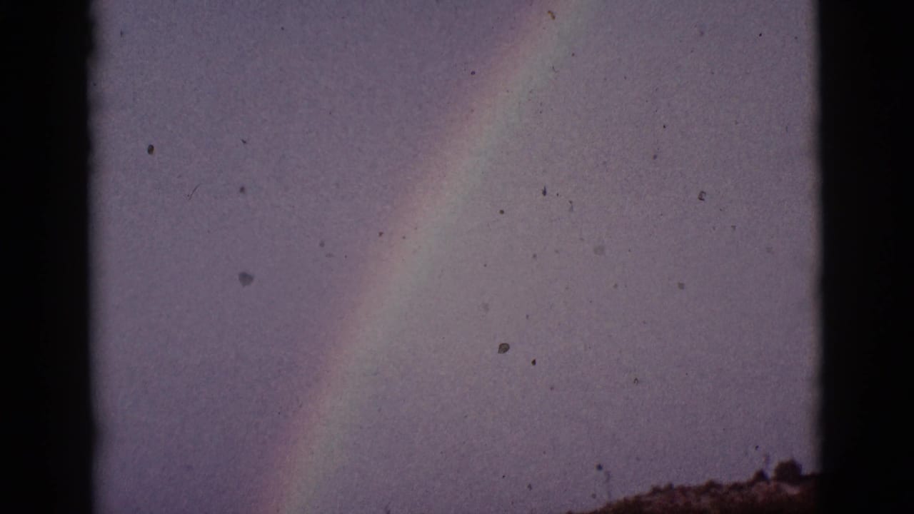 Rainbow segment in a muted sky with dark film edge and a low horizon.