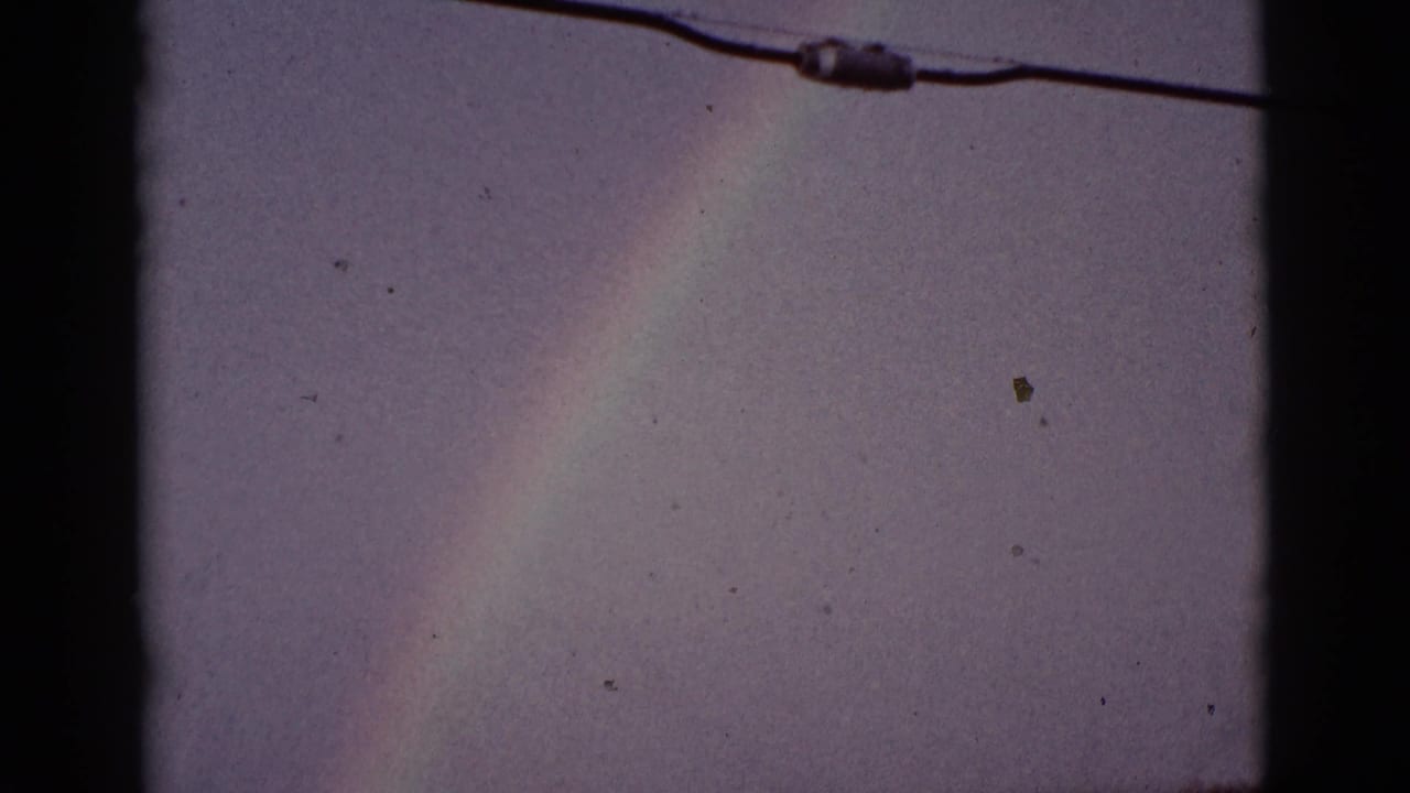 Rainbow in a cloudy sky with an overhead wire near the top of frame.