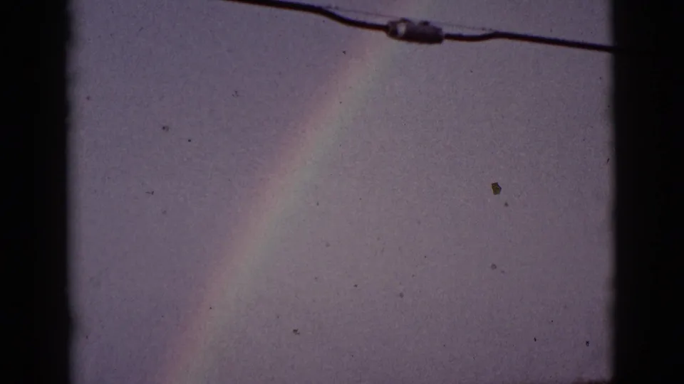 1965 8mm Tucson-area frame with a rainbow column in a muted sky and an overhead utility wire crossing near the top.