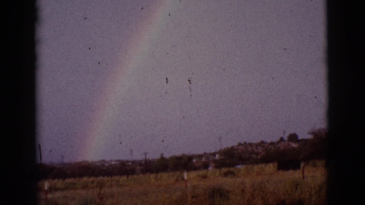 Rainbow over a dry field seen through dark window-frame edges.