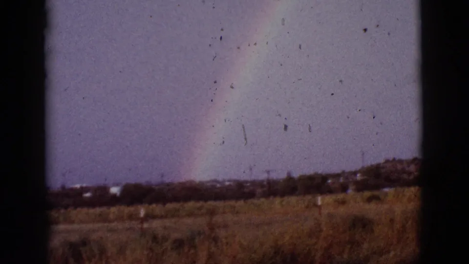 Faded 8mm frame of a rainbow over a dry Arizona field, with dark window borders and dust marks visible in the scan.