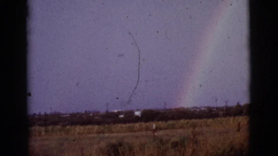 Final 1965 home-movie frame showing a rainbow over a dry field near Tucson, with distant brush and visible film wear.