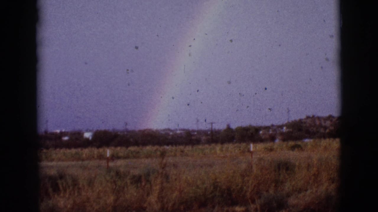 Partial rainbow above a dry field, seen through dark vertical film borders.