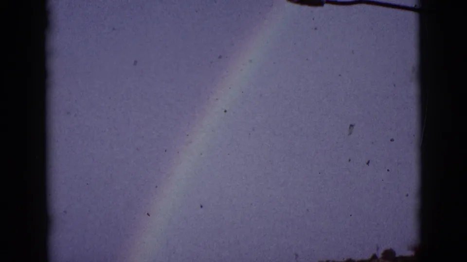 The final 1965 8mm frame isolates the rainbow against a hazy Tucson-area sky, with only a narrow dark horizon at the bottom.