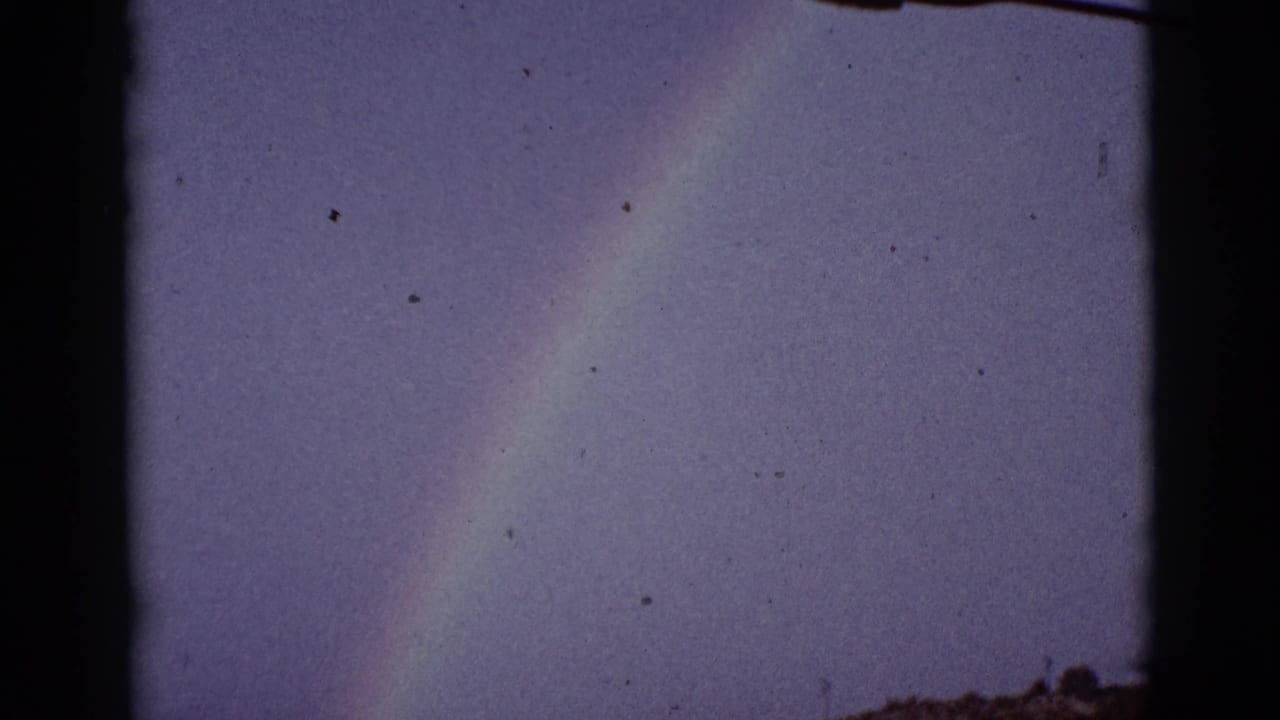 Faint rainbow over a grassy rural field with dark 8mm frame edges.