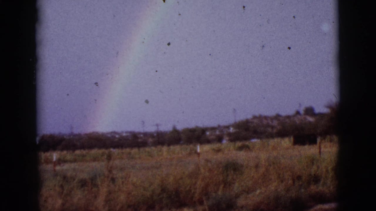 Rainbow over a dry field seen through a dark window frame.
