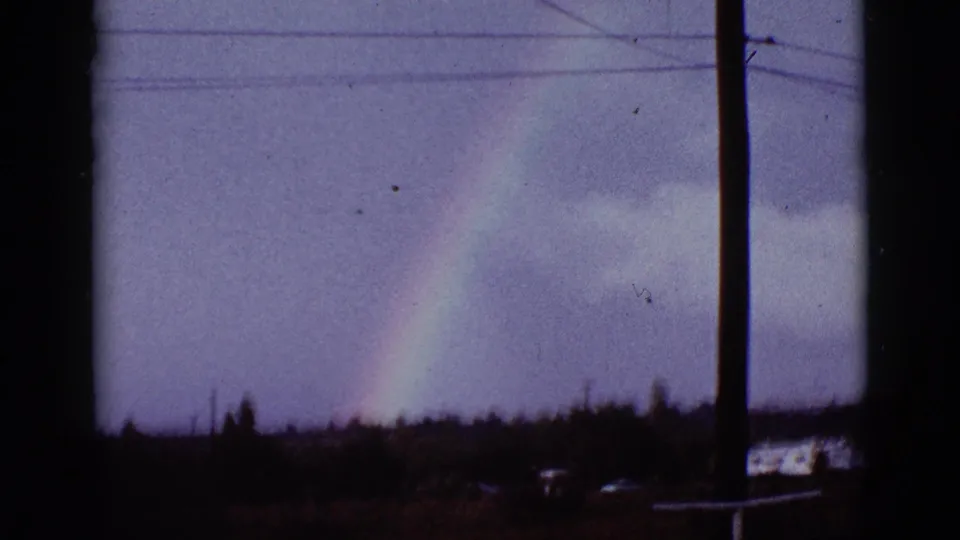 1965 Tucson-area frame showing a rainbow against sky, crossed by utility wires and bordered by dark window or post edges.