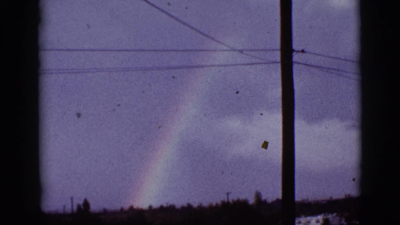 Rainbow over a cloudy low horizon, seen through dark window framing with power lines.