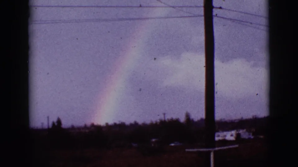 1965 8mm Tucson metadata frame showing a rainbow near a utility pole and overhead lines above a dark low landscape.