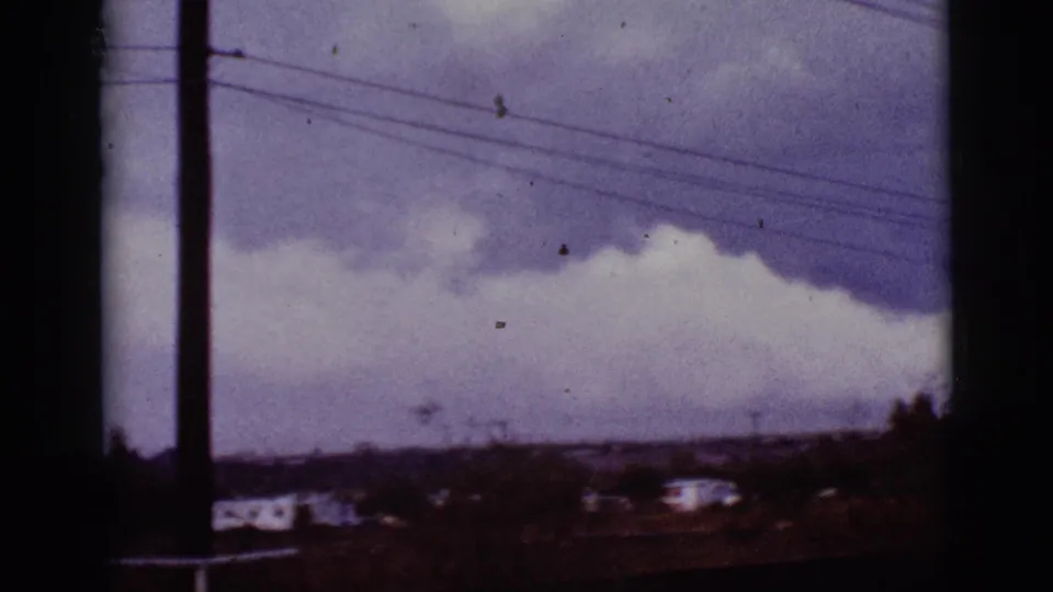 1965 8mm view near Tucson showing dark clouds, power lines, distant houses, and dry vegetation.