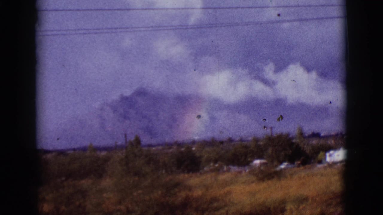 1965 Tucson-area 8mm frame showing a faint rainbow over distant mountains, with dry grass, houses, utility lines, and dark window-like borders.
