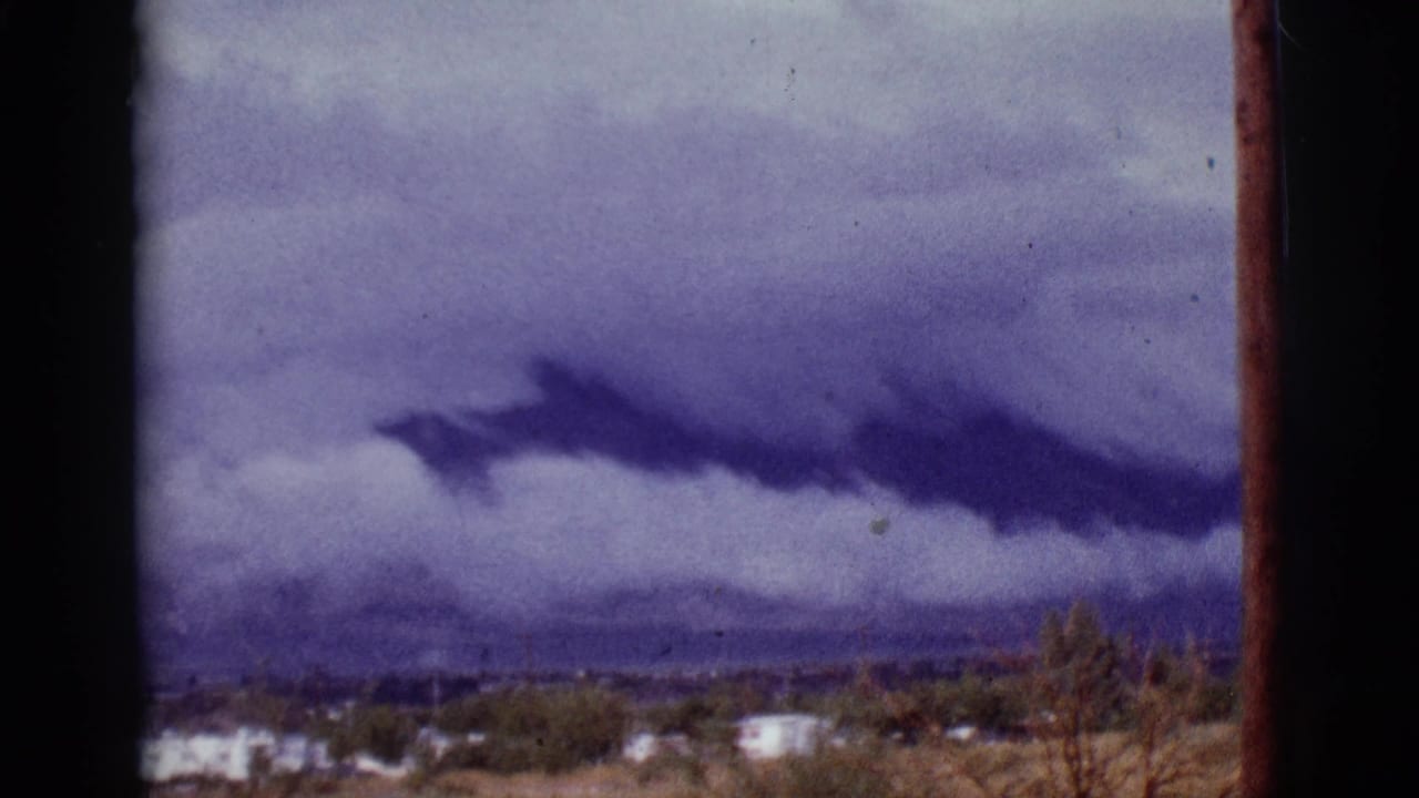 Storm clouds over desert trailers and distant mountains, framed by dark film edges.