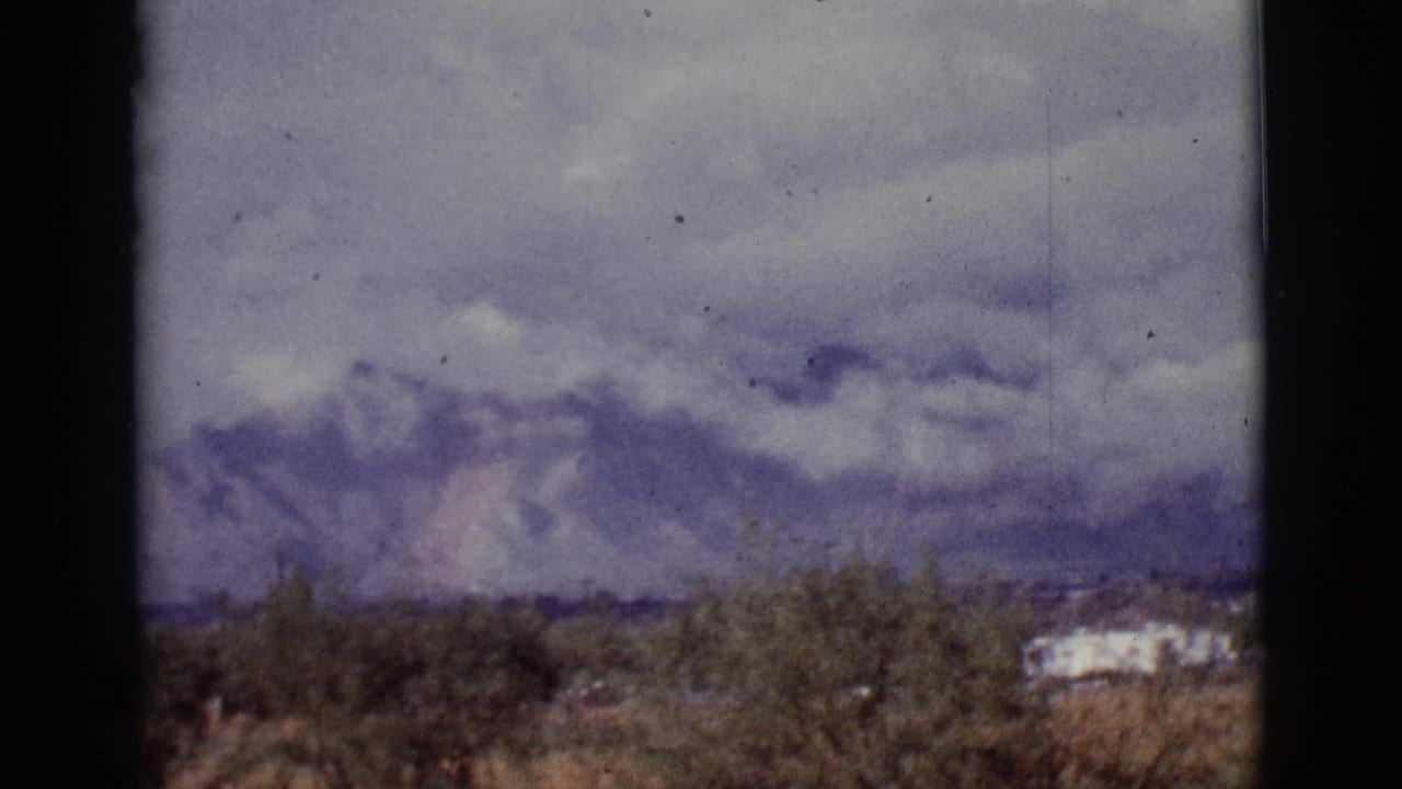Desert brush and distant mountains under a cloudy sky with film gate edges.