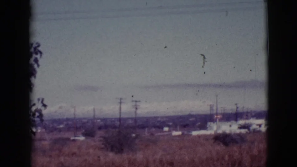 Tucson-area desert outskirts with utility poles, scattered low buildings, and a hazy overcast mountain horizon.