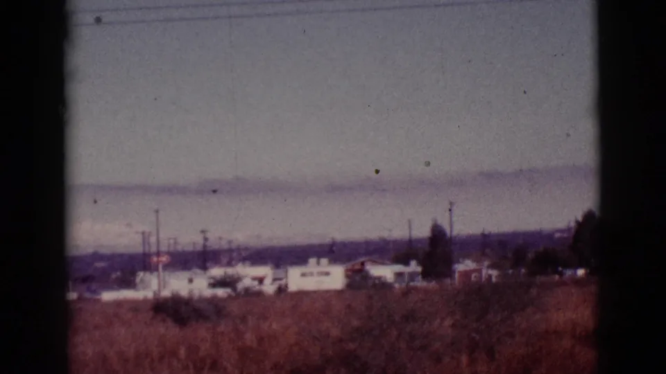 Distant Tucson trailer-park structures and utility poles appear across open desert scrub in the 1965 home movie footage.