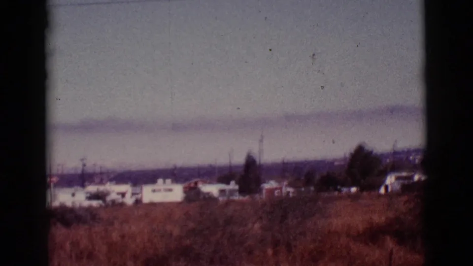 White mobile homes and utility poles line the edge of dry Tucson desert brush, with hazy hills behind them.