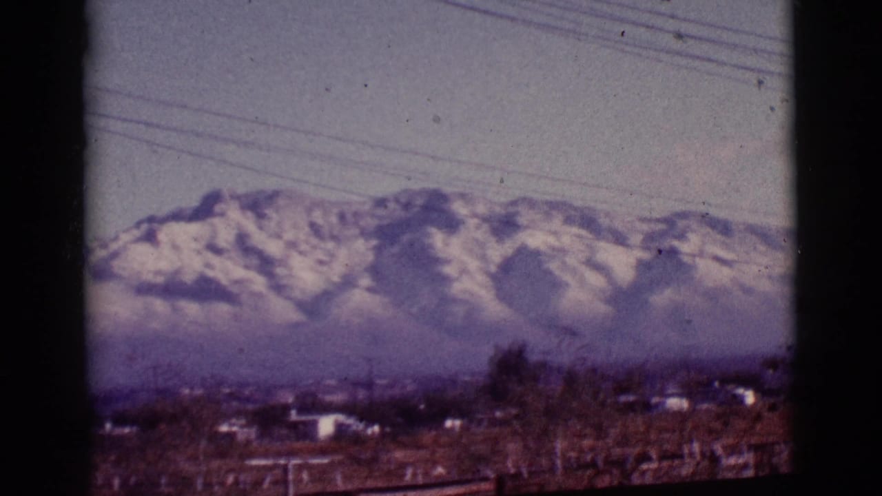 Distant snowy mountains and hazy sky framed by dark vertical edges with power lines overhead.