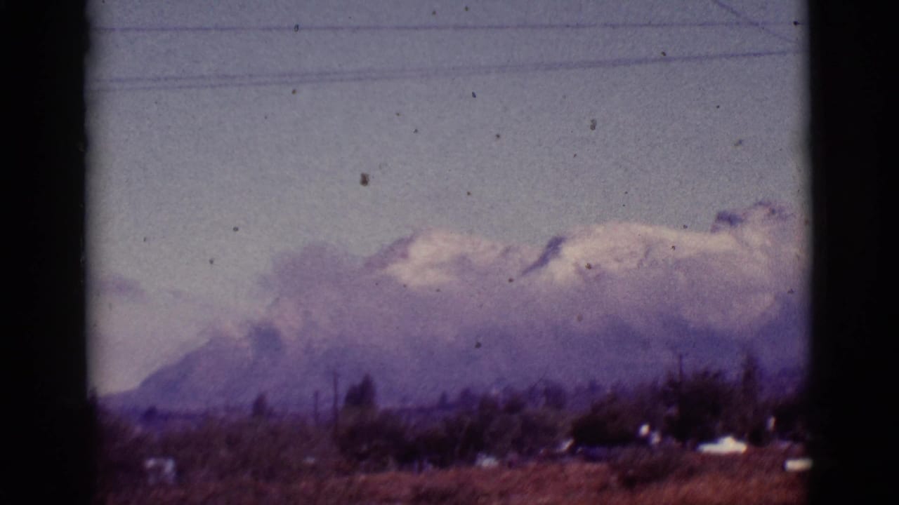 1965 8mm view near Tuscon, Arizona, showing hazy snow-capped mountains behind rural grassland and overhead utility lines.